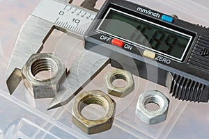 Digital electronic caliper with used nuts on a background of storage box