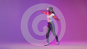 Digital Entertainment. Happy Black Woman In VR Glasses Walking On Purple Background