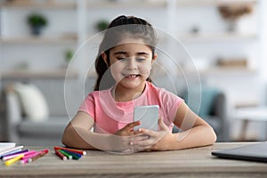 Digital Entertainment. Portrait Of Cute Little Girl Relaxing With Smartphone At Home