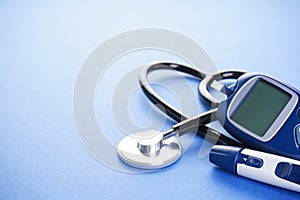 Digital glucometer and lancet pen and stethoscope on blue background with space for text. Diabetes concept, medical technology