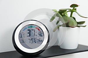 Digital hygrometer with thermometer and green plant on shelf, closeup