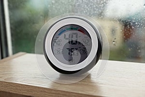 Digital hygrometer with thermometer near window on rainy day, closeup