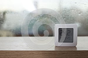 Digital hygrometer with thermometer near window on rainy day. Space for text