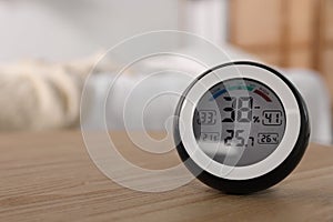 Digital hygrometer with thermometer on wooden table indoors. Space for text