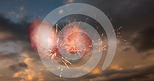 Digital image of red fireworks exploding in the sky with clouds during sunset