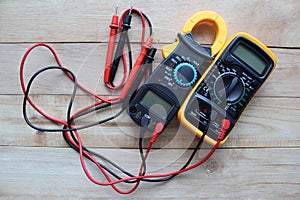 Digital multimeter, clamp-on meter with probes, electrical measuring instruments isolated on wooden background closeup.