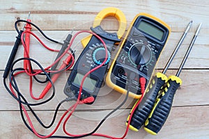 Digital multimeter, clamp-on meter with probes, electrical measuring instruments, and screwdrivers isolated on wooden background