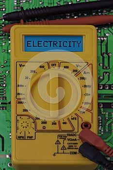 Digital multimeter multitester on a circuit board with the word electricity