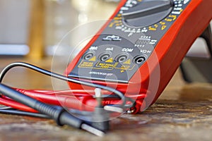 Digital multimeter with probes on a wooden table in the workshop