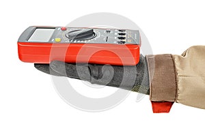 Digital multimeter with red rubber protective case lies on palm of electrician hand in black protective glove and brown uniform