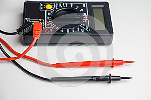 Digital multimeter with test leads on a white table. A multimeter is an electronic measuring instrument