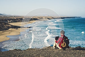 Digital nomad lifestyle concept with adult man sit down on the ground with scenic view of beach and ocean inbackground - work with photo