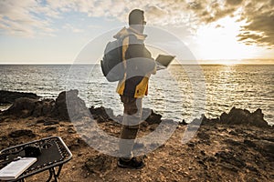 Digital nomad traveler man at work lokking an amazing golden sunset on the ocean. camera and laptop and beautiful lifestyle in