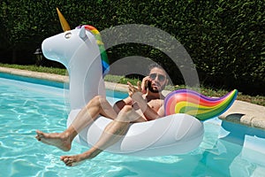 Digital nomad wearing sunglasses talking on the phone backwards on a unicorn inflatable ring in a swimming pool
