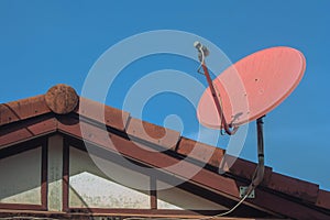 Digital satellite television receiving dish setting on top of house roof with blue sky in background.