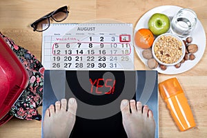 Digital scales with female feet sign `yes!` surrounded by calendar, summer accessories and plate with healthy food.