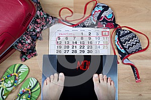 Digital scales with female feet on them and sign`no!` surrounded by calendar and summer holiday accessories.