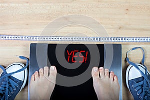 Digital scales with female feet on them and sign surrounded by gymshoes and measuring tape.