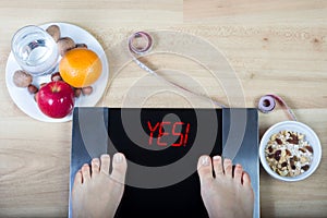 Digital scales with female feet on them and sign `yes!` surrounded by healthy food.