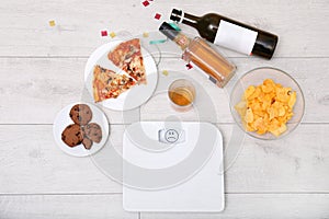 Digital scales, junk food and alcohol on wooden floor after party