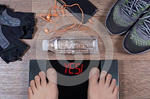 Digital scales with male feet on them and sign yes! surrounded by gymshoes, sport gloves, water