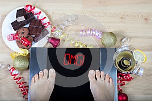 Digital scales with woman feet on them and sign sign`OMG!` surrounded by christmas decorations and unhealthy food photo