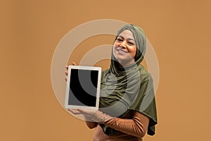 Digital tablet with black screen in hands of arab woman in hijab, smiling and demonstrating device with space for design