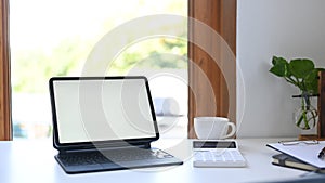 Digital tablet with blank screen, calculator, coffee cup and documents on white table.