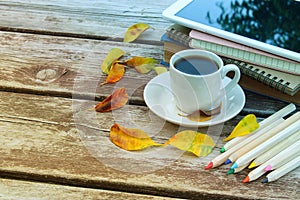 Digital tablet, books, colorfull pencils and cup of coffee on old wooden table outdoor in the park.