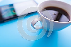 Digital tablet computer and cup of coffee on blue backgroubnd. Simple workspace or coffee break with web surfing