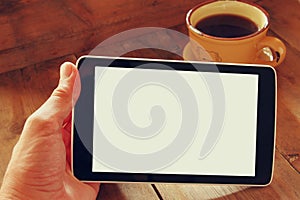 Digital tablet computer with isolated screen in male hands over wooden table background and cup of coffee