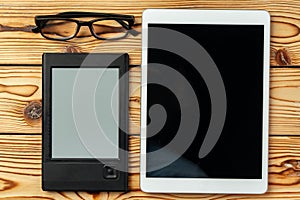 Digital tablet and electronic reader book with glasses on wooden background top view