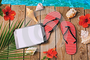 Digital tablet, flip flops and hibiscus flowers on wooden background. Summer holiday vacation concept. View from above