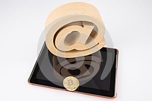 Digital tablet with gold coin bitcoin currency and big arobase sign