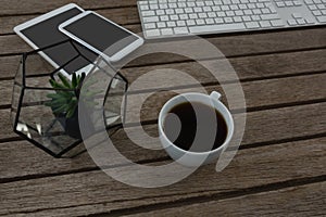 Digital tablet, mobile phone, mouse, pot plant, keyboard and black coffee on wooden plank