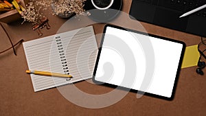 Digital tablet, notebook and coffee cup on brown background.