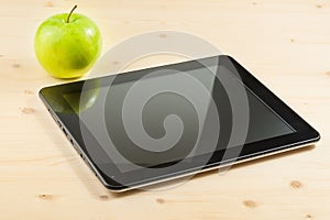 Digital tablet pc near green apple on wood table