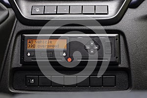 Digital tachograph display reads Vehicle Overspeed. No personal data. Tachograph in a van