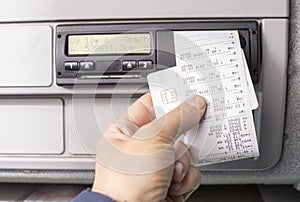 Digital tachograph and drivers hand holding print with driving times of the day