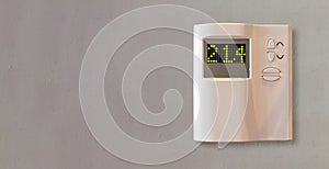 Digital thermostat on grey empty wall background. Home heating temperature control device close up