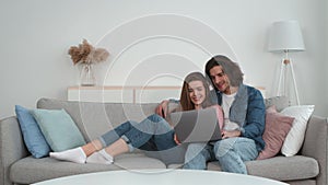 Digital tv concept. Young married couple relaxing at home, watching movies on laptop together, embracing on sofa