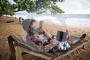 The digital vacationer lying on the bench by the sea makes a call while using his PC photo