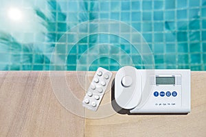 Digital water tester equipment and pool tester tablet on swimming pool edge with space on blue water background