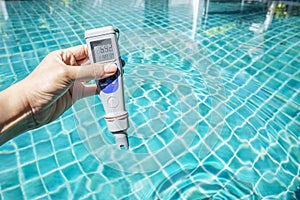 Digital waterproof and temp pocket tester in girl hand over blue swimming pool water,