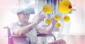 Digitally generated image of emojis flying against man using VR glasses sitting on wheelchair