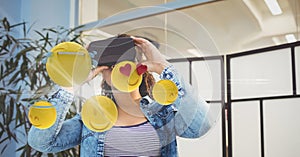 Digitally generated image of emojis flying against woman using VR glasses at home