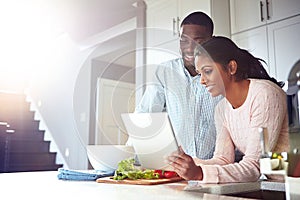 Digitizing the cooking experience. a young couple using a digital tablet while preparing a healthy meal together at home