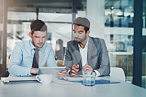 Digitizing a financial discussion. two young businessmen using a digital tablet while going through paperwork together