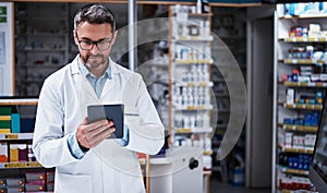 Digitizing his dispensary duties. a handsome mature pharmacist using a digital tablet in a pharmacy.