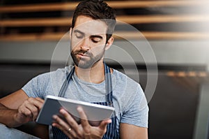 Digitizing his managerial duties. a young man using a digital tablet while working at a coffee shop.